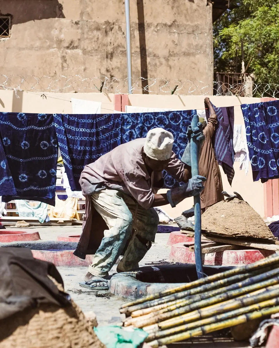 Dyer stirring the indigo vat, with fabrics drying behind him